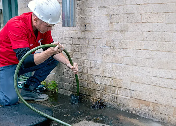 A worker in a red shirt is clearing debris near the drain with a hose